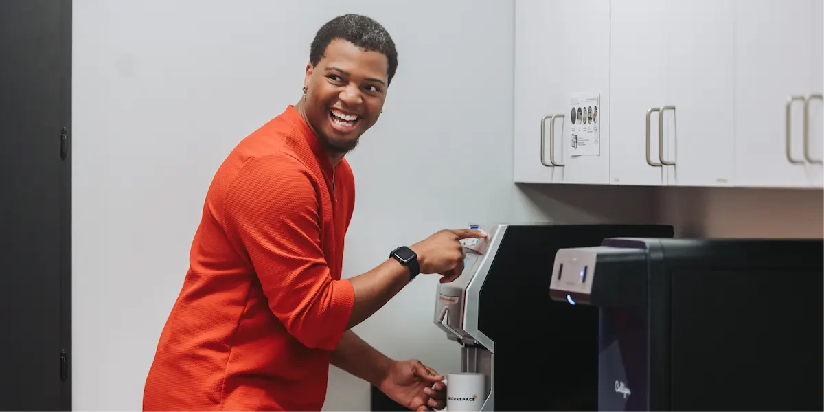 Man smiling while using a coffee machine in an office kitchen area.