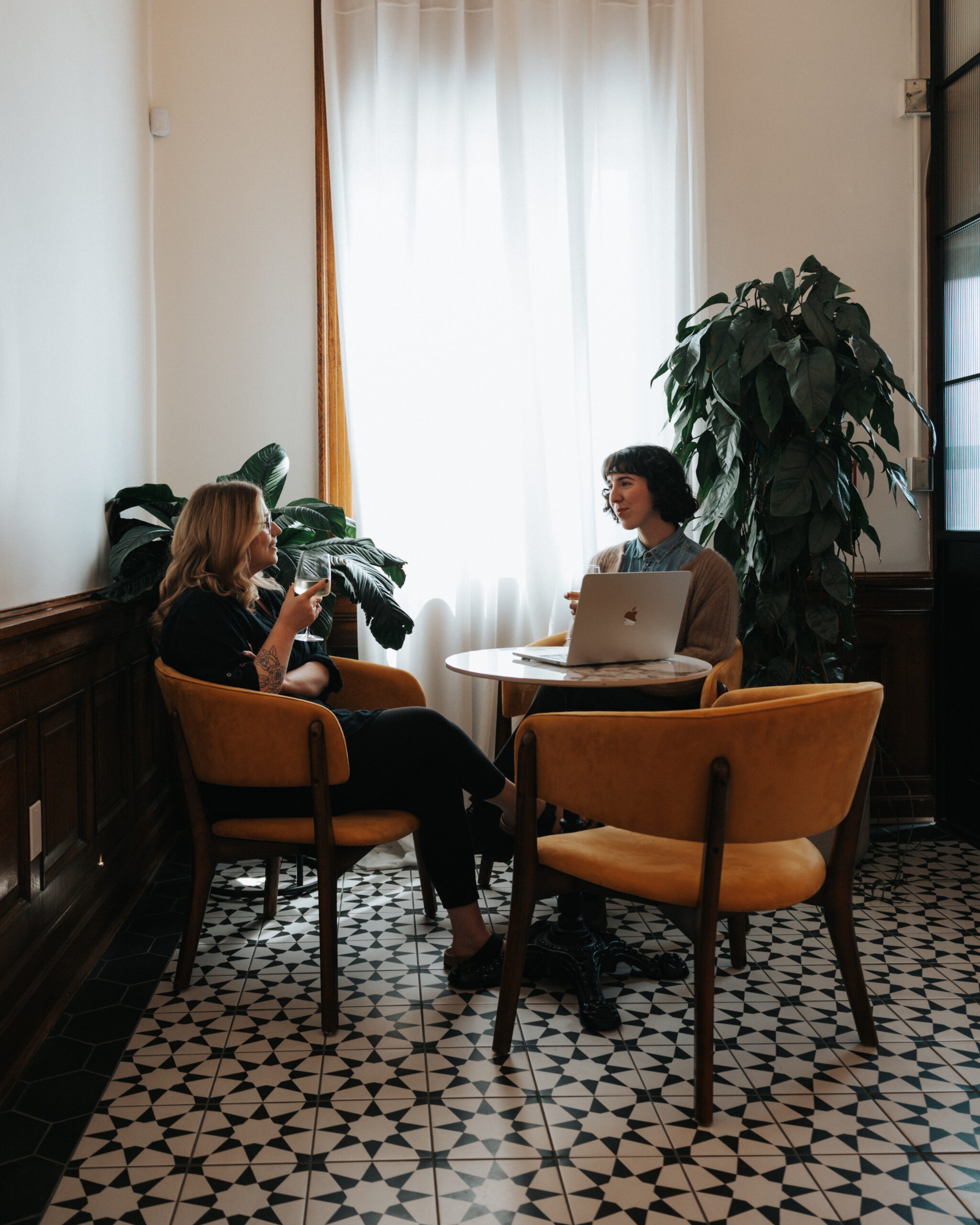 Two Den 1880 members in conversation at a cafe table, one with a laptop open